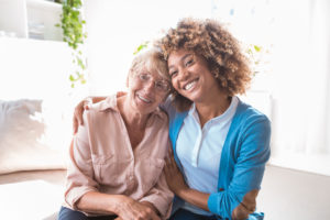 Cheerful home caregiver embracing senior woman