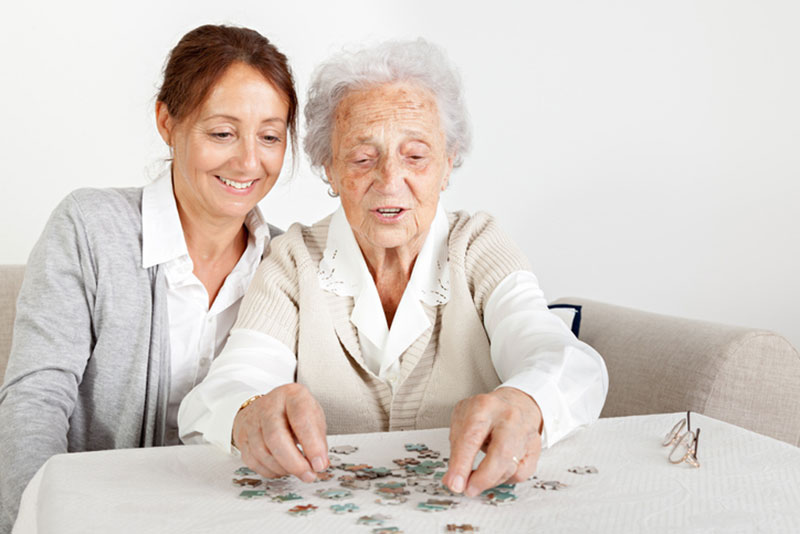 A woman puts together a puzzle with her elderly mother, one of many engaging activities for someone with dementia.