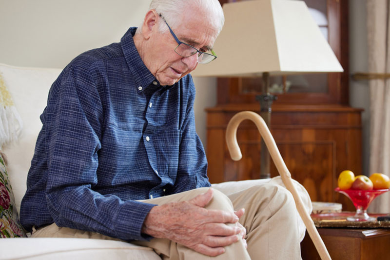 An older man rubs his sore knee while prepping for joint replacement surgery