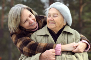 An adult woman hugs her aging mother, knowing it’s important to prioritize self-care for family caregivers.