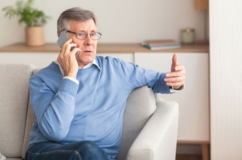 An older man is cautious when he speaks on the phone because he knows about scams targeting seniors.